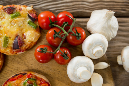 Overhead view of pizza, tomato, and garlic on a wooden tray on a wooden trayの写真素材