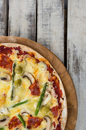 Overhead view of a italian pizza in a chopping board on a wooden plankの写真素材