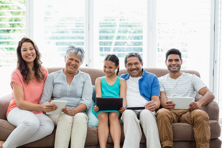 Portrait of multi-generation family using digital tablet in living room at home