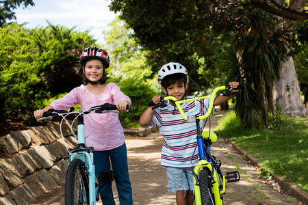 Portrait of smiling children standing with bicycle in park on a sunny dayの写真素材