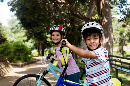 Portrait of smiling children standing with bicycle in park on a sunny day