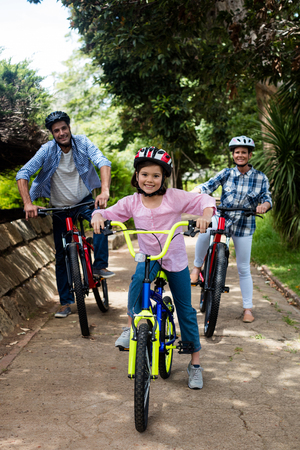 Portrait of happy parents and daughter standing with bicycle in park on a sunny dayの写真素材