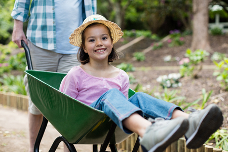 Father pushing daughter in wheelbarrow at parkの写真素材