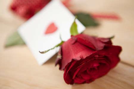 Red rose wrapped in ribbon and heart printed envelope against wooden backgroundの写真素材
