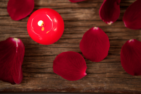 Red wax candles surrounded with rose petals against wooden backgroundの写真素材