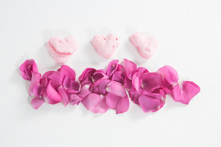 Heart shaped confectionery and pink rose petals on white backgroundの写真素材