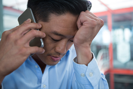 Sad businessman talking on mobile phone in officeの写真素材
