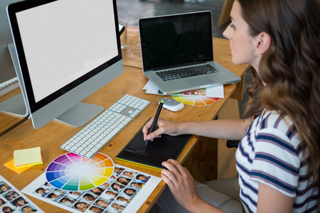 Female graphic designer using graphics tablet at desk in office