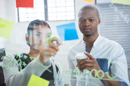 Business colleagues reading sticky notes on glass in officeの写真素材