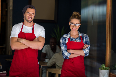 Portrait of smiling waitress and waiter standing with open sign board outside cafÃ©の写真素材