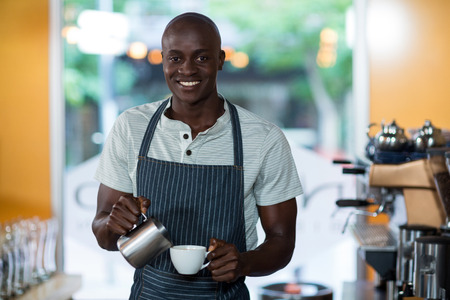 Portrait of waiter making cup of coffee at counter in cafeの写真素材