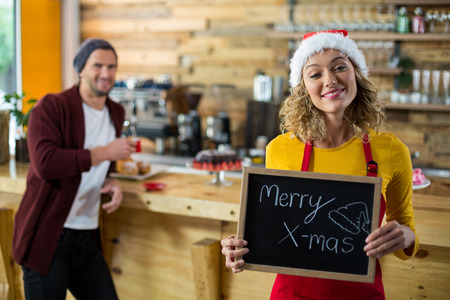 Portrait of smiling waitress standing with merry x mas sign board in cafeの写真素材