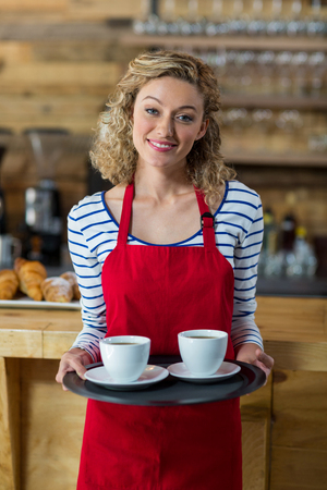 Portrait of smiling waitress standing with cup of coffee in cafÃ©の写真素材