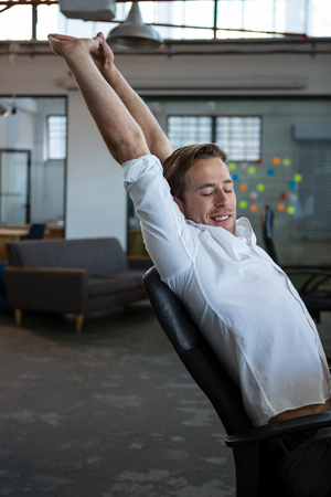 Businessman stretching at desk in officeの写真素材