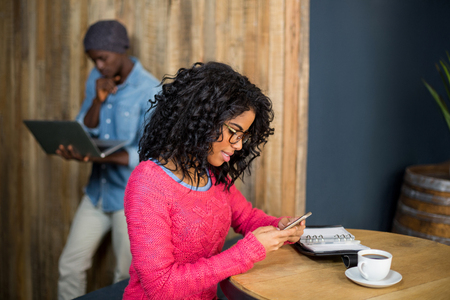 Woman sitting at table and using mobile phone while having a coffee in cafÃ©の写真素材