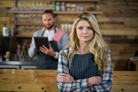 Portrait of waitress standing with arms crossed at counter in cafÃ©