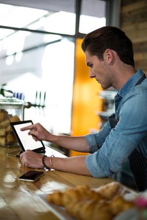 Waiter standing at counter using digital tablet in cafÃ©