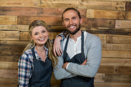 Portrait of smiling waiter and waitress standing against wooden wall in cafeの写真素材