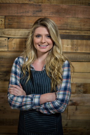 Portrait of waitress standing with arms crossed against wooden wall in cafÃ©の写真素材