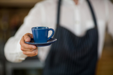 Mid-section of waiter offering a cup of coffee in cafÃ©の写真素材