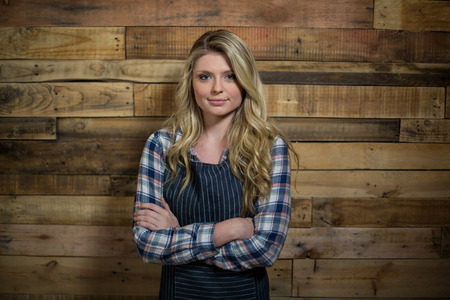 Portrait of waitress standing with arms crossed against wooden wall in cafÃ©の写真素材