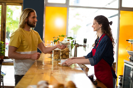 Smiling customer paying bill by cash at counter in cafÃ©