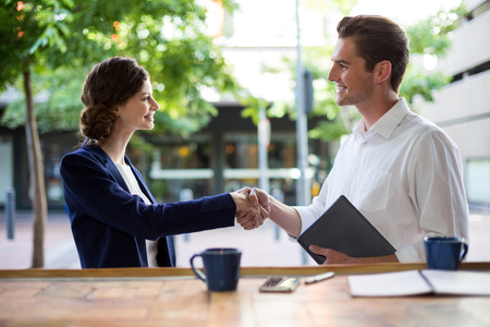 Businesswoman shaking hands with businessman at counter in cafeの写真素材