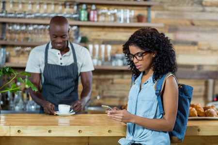 Woman using mobile phone while waiter standing in background at cafÃ©の写真素材