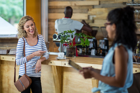Woman smiling while using mobile phone at counter in cafÃ©の写真素材