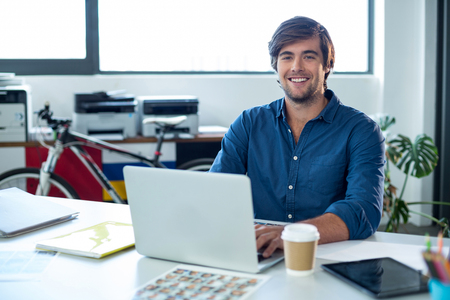 Portrait of male graphic designer working on laptop in officeの写真素材