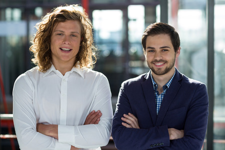 Two male business executives standing with arms crossed in officeの写真素材