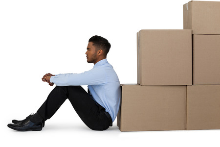 Thoughtful businessman leaning on cardboard boxes against white backgroundの写真素材