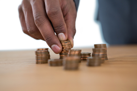 Hand of businessman holding stack of coins on table