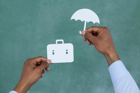 Man protecting paper cut out briefcase with umbrella on green backgroundの写真素材