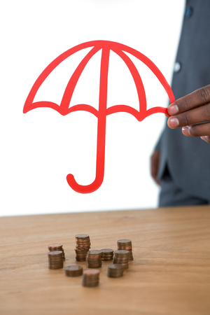 Mid section of businessman protecting stack of coins with umbrella at deskの写真素材
