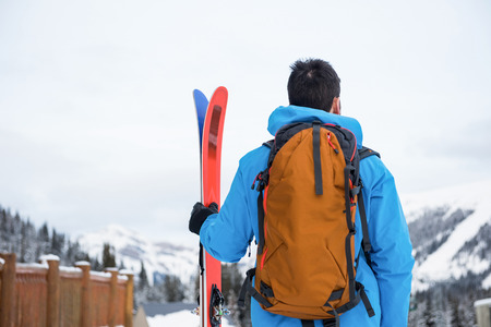 Rear view of skier standing with ski on snow covered mountainsの写真素材