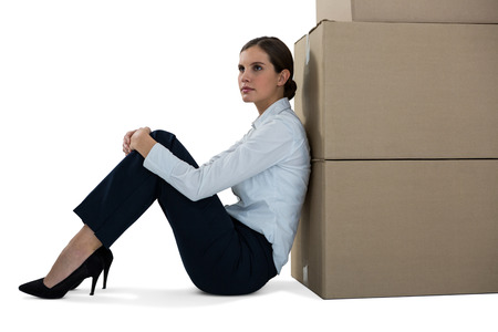 Thoughtful businesswoman leaning on cardboard boxes against white backgroundの写真素材