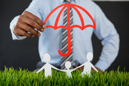 Mid section of businessman protecting paper cut out family with umbrellaの写真素材