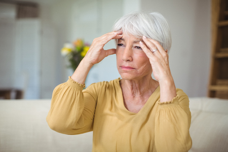 Senior woman suffering from head ache in living room at homeの写真素材