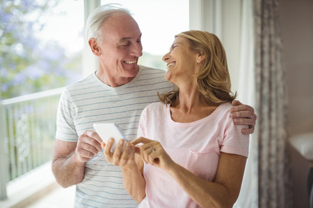 Happy senior couple using mobile phone in balcony at homeの写真素材