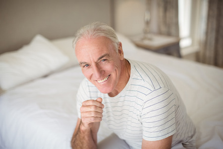 Portrait of happy senior man sitting on bed in bedroom at homeの写真素材