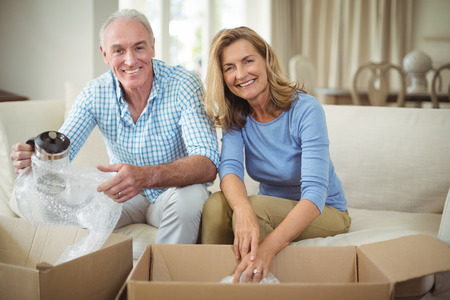 Portrait of smiling senior couple unpacking carton boxes in living room at new homeの写真素材