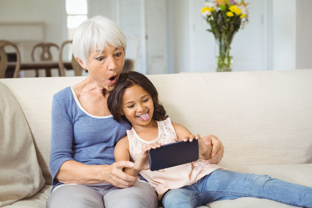 Granddaughter and grandmother taking selfie on mobile phone in living room at homeの写真素材