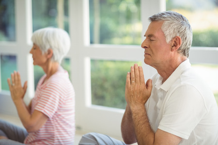 Senior couple performing yoga on exercise mat at homeの写真素材