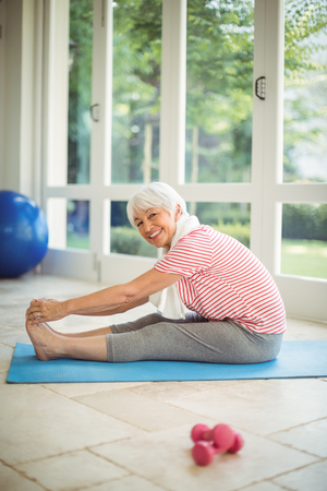 Portrait of happy senior woman performing stretching exercise at homeの写真素材