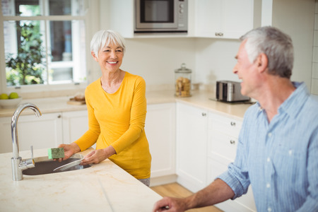 Happy senior woman interacting with man in kitchen while washing dishesの写真素材