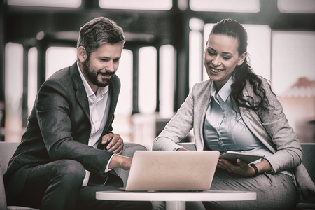 Businesspeople sitting and discussing over laptop in officeの写真素材