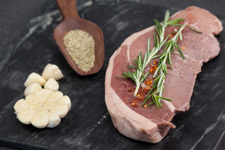 Sirloin chop, garlic and spices on black slate plate against wooden backgroundの写真素材