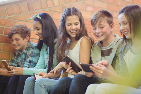 Group of smiling school friends sitting on staircase using mobile phone at schoolの写真素材