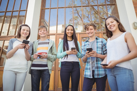Portrait of smiling school friends using mobile phone in campus at school